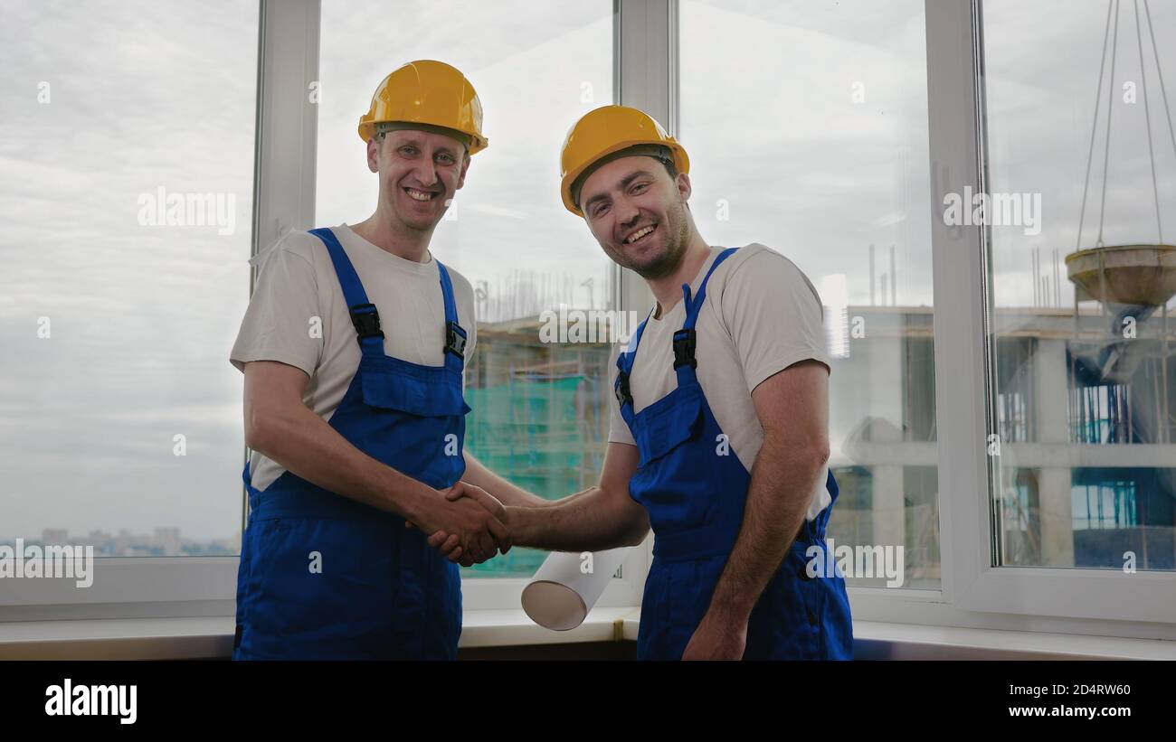 Handsome construction workers in protective helmets shaking hands. Stock Photo