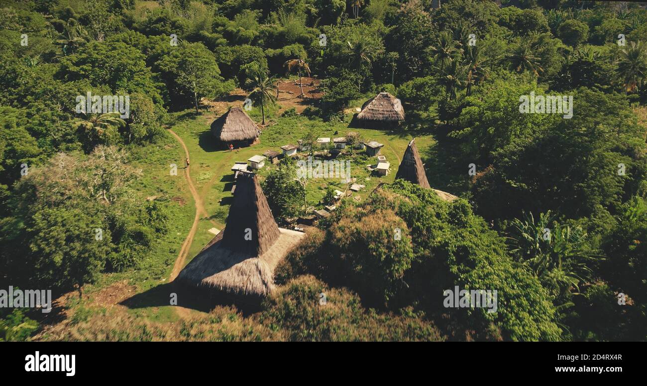 Traditional houses of Indonesia village at tropical green landscape aerial view. Unique buildings with hives, path at greenery grassy valley. Cinematic long-held tradition countryside of Sumba Island Stock Photo