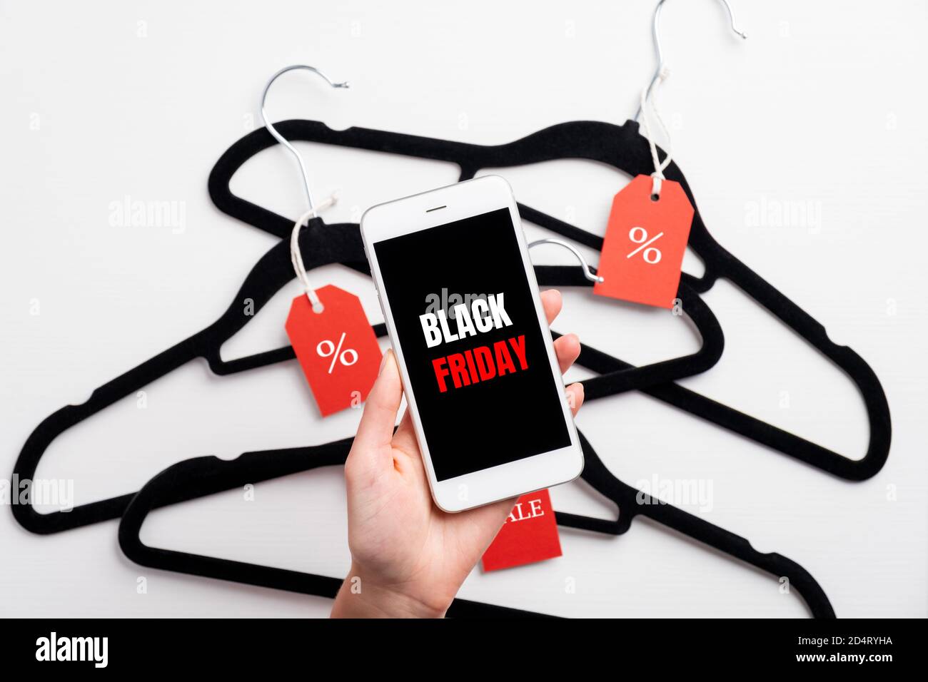 Black Friday alert on mobile smartphone in female hand. Coat hangers with red labels on background. Stock Photo