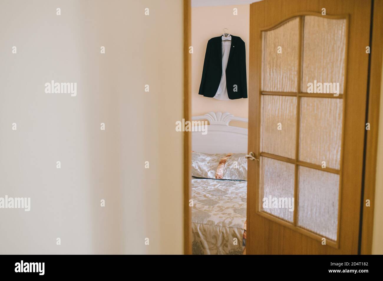 View through the open door beautiful black suit white groom's shirt hanging on a hanger. Stock Photo