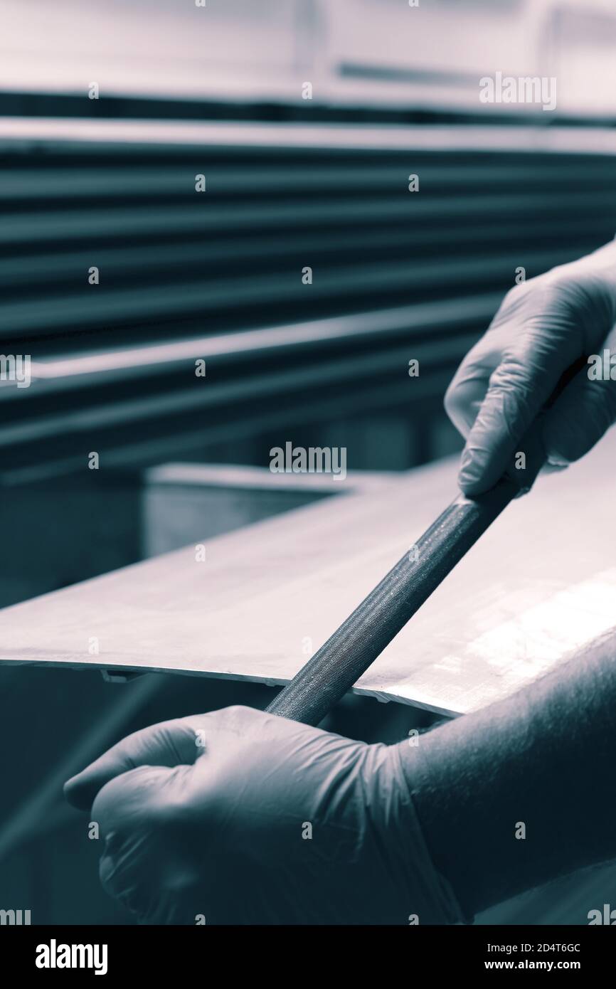 Man filing deburring a metal panel with a file. With colout toning ...