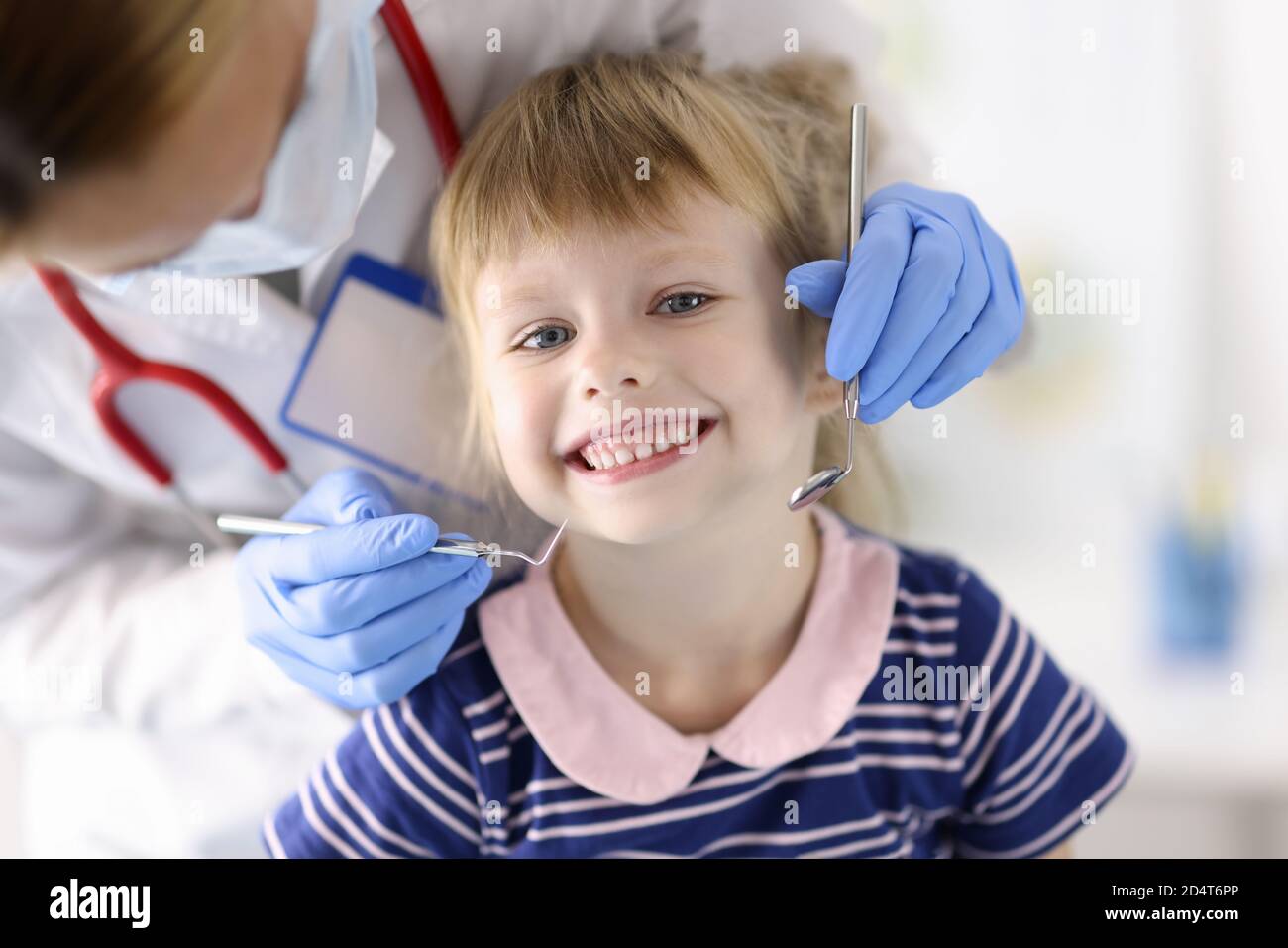 Dentist doctor examines teeth of little smiling girl in clinic Stock