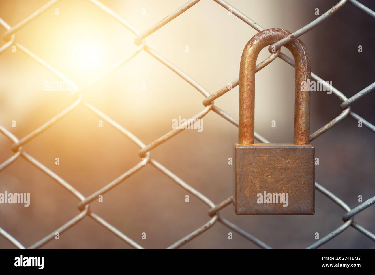 An old and rusty lock hanging on the iron mesh fence. Stock Photo