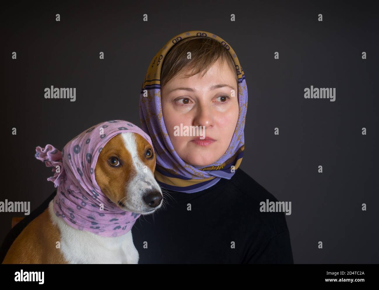 Nice low key portrait of beautiful Caucasian woman with lovely basenji dog both wearing headscarfs Stock Photo