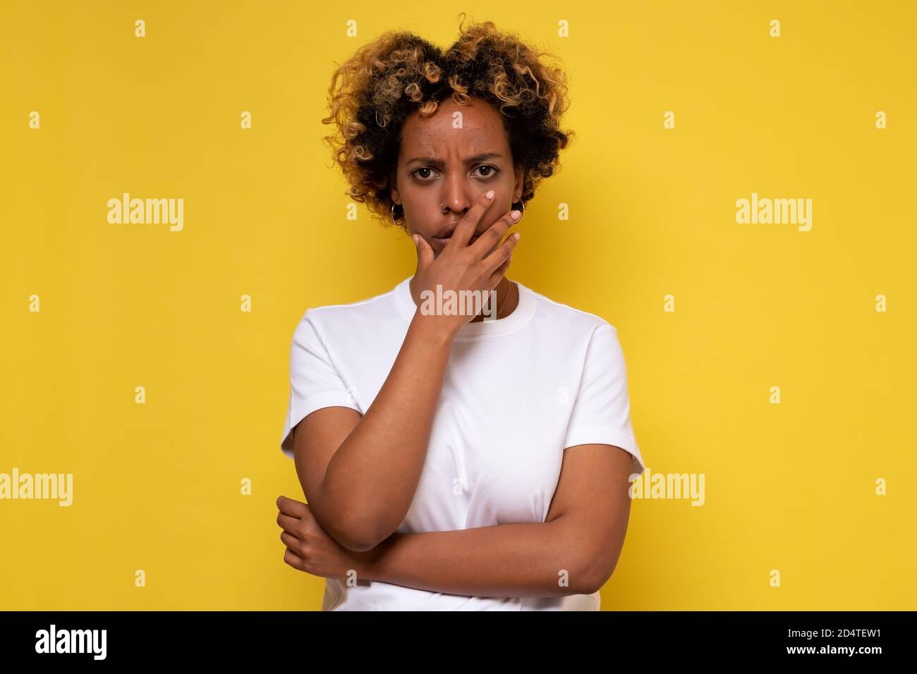 Lovely confused african woman with curly hair against yellow wall. Stock Photo