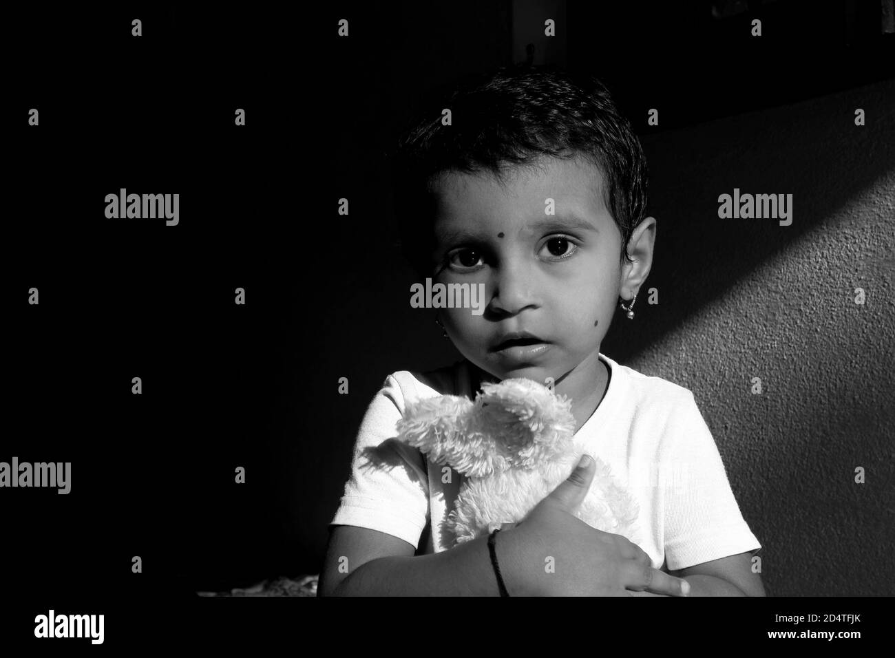 a closeup shot of Indian girl child holding doll in morning sunlight monochrome stock photo, Kalaburagi, Karnataka/India-October 09 2020 Stock Photo