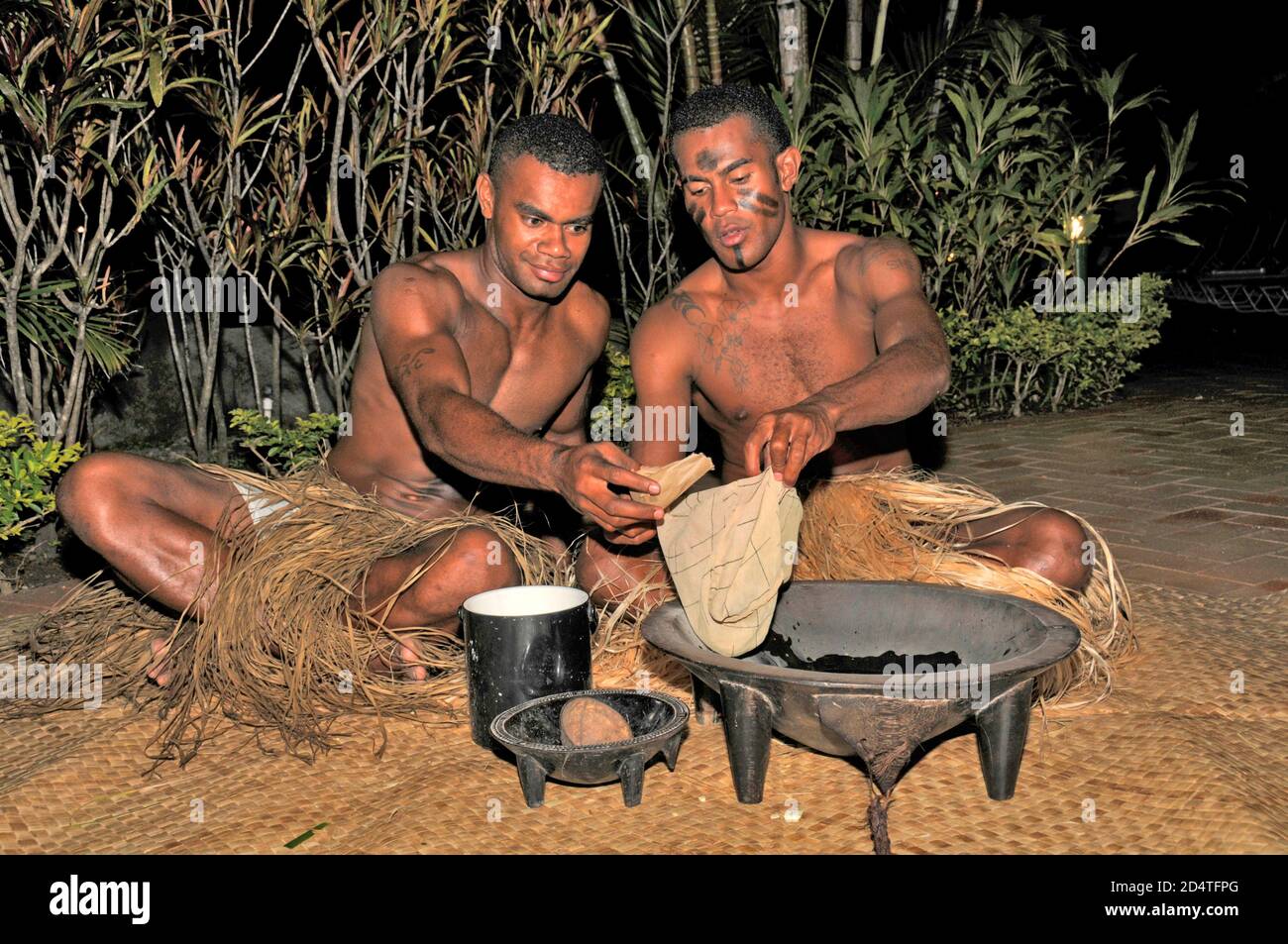 Two Fijians squat on matting at a tourist show to serve Fiji's national drink, Yaqona, also called Kava in Fiji in the South Pacific.   Yaqona or Kava Stock Photo