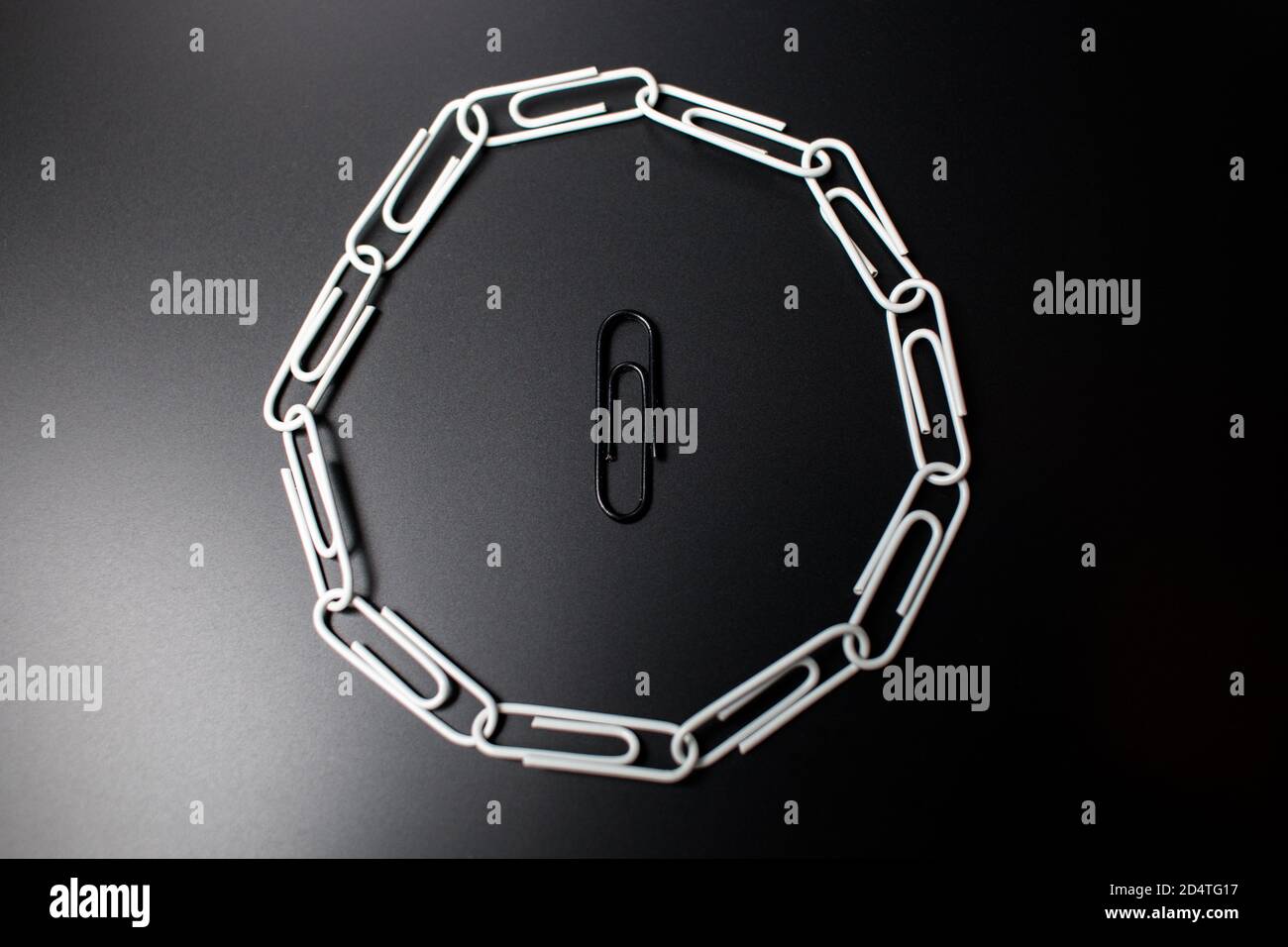 A circle of paperclips with one in the middle that is not fitting in and is surrounded. Symbolic representation of not fitting in the group and being Stock Photo