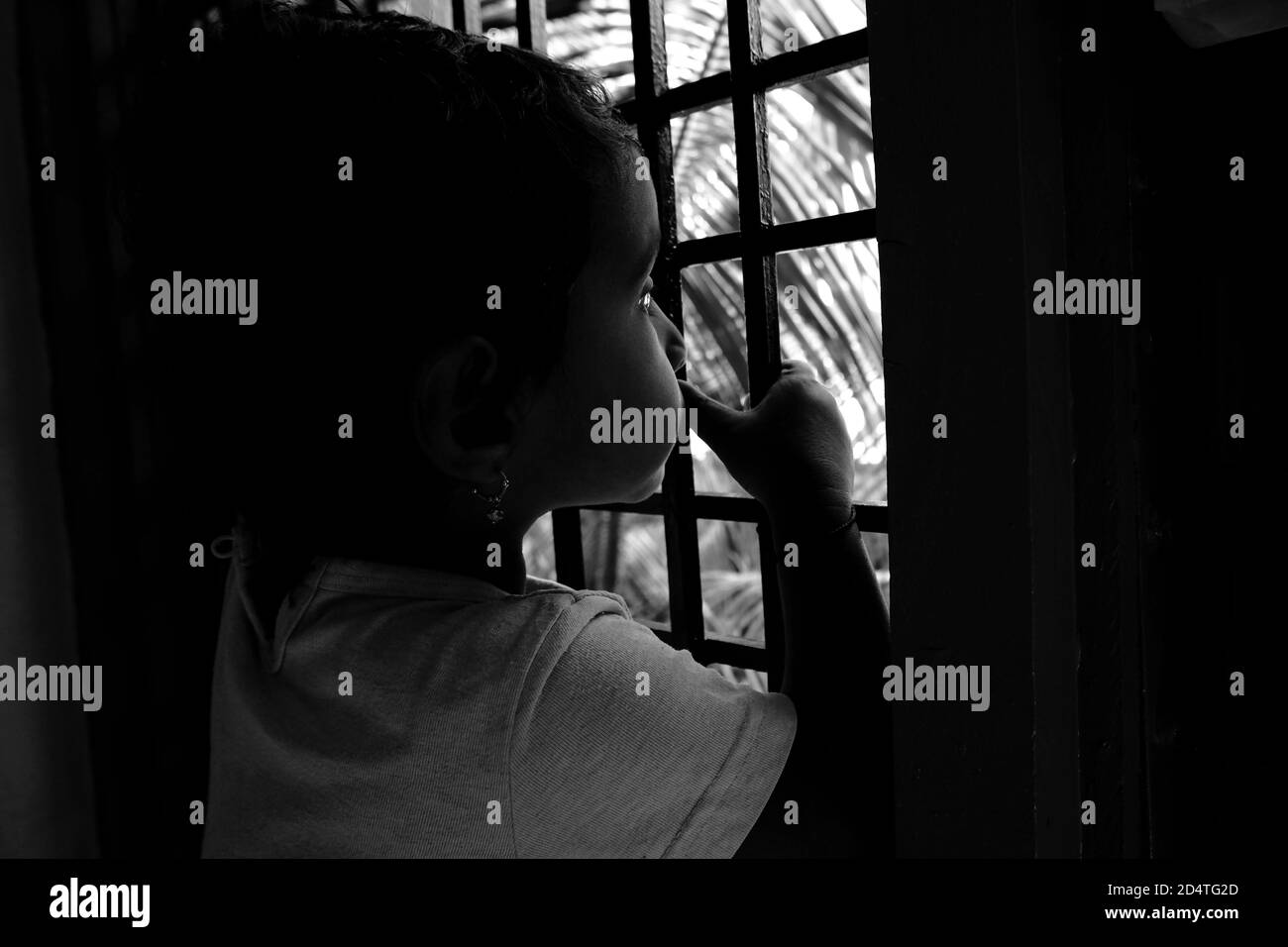 a close shot of Indian girl child peeping in window outside the nature in monochrome photo, Kalaburagi, Karnataka/India-October 09 2020 Stock Photo