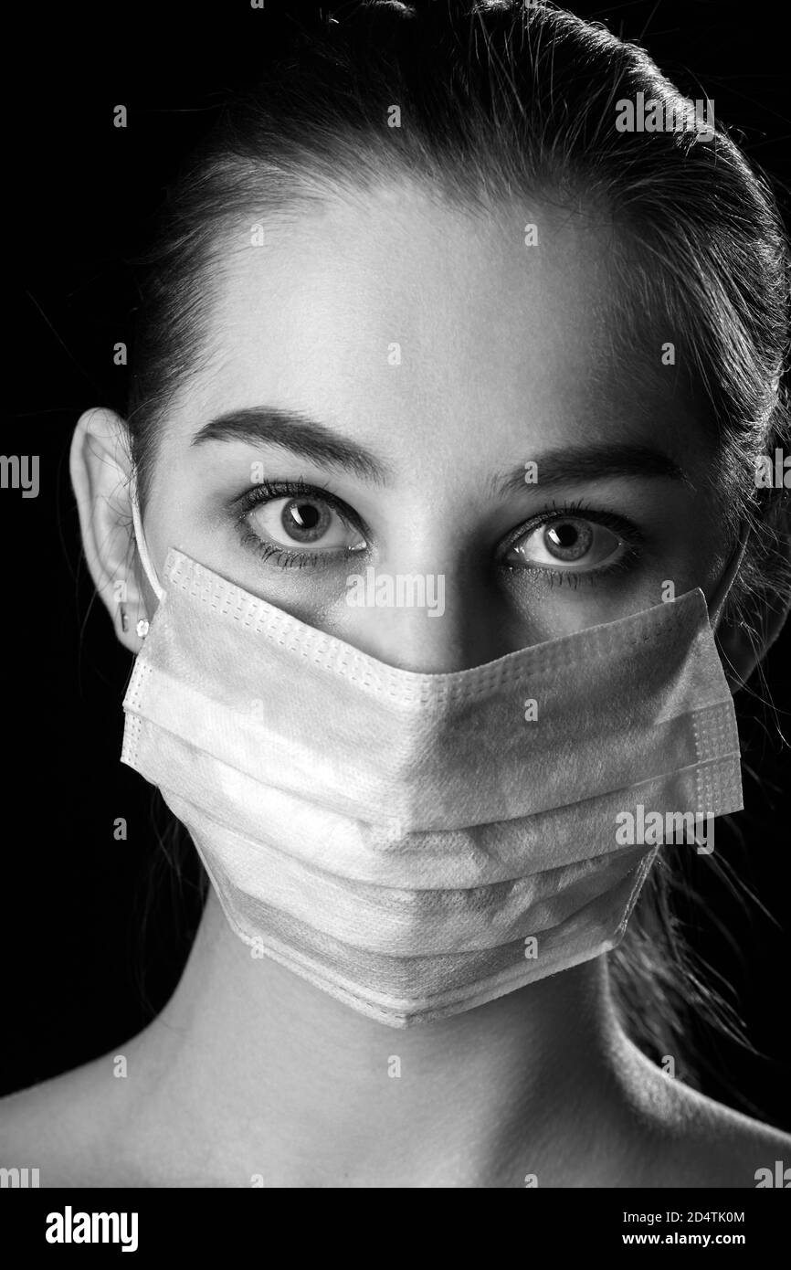 young sad woman in medical mask on black background looking at camera ...