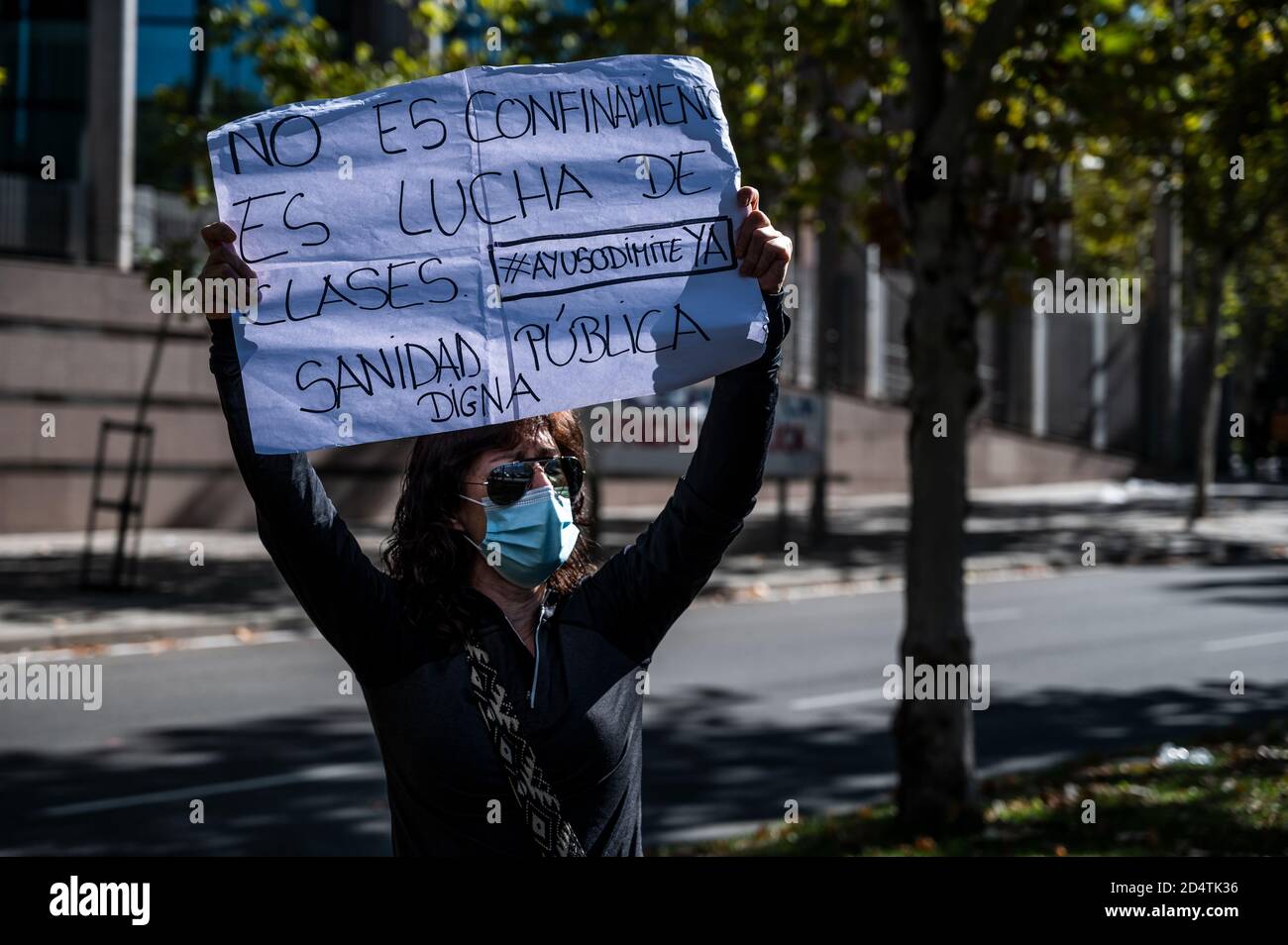 Madrid, Spain. 11th Oct, 2020. A woman holds a placard reading 'It is not confinement, it is class struggle. Ayuso resign now. Decent public health', as residents of the Vallecas neighborhood of Madrid protest in front of the Regional Community Parliament demanding the resignation of regional president Isabel Diaz Ayuso for the negligent management of the coronavirus crisis and in support of the public health system. Credit: Marcos del Mazo/Alamy Live News Stock Photo