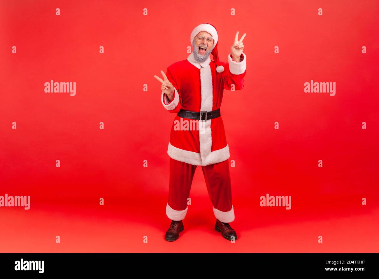 Full length portrait of positive funny gray bearded man in santa claus costume winking showing peace gesture with fingers, free and optimistic waiting Stock Photo