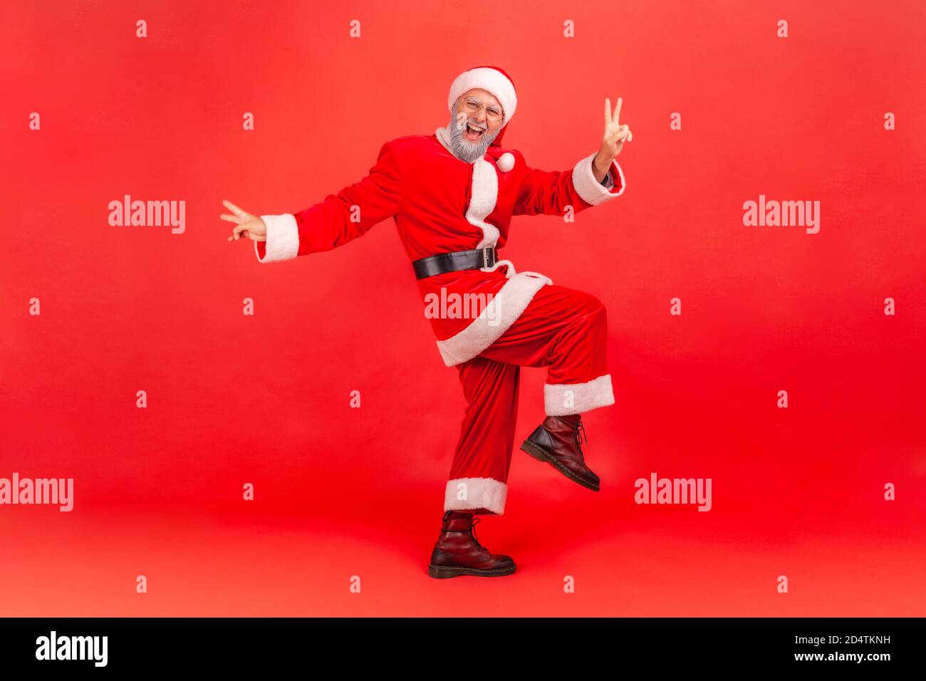 Full length portrait of happy positive man in santa claus costume jumping showing v gesture with fingers, celebrating victory, winter holidays coming. Stock Photo