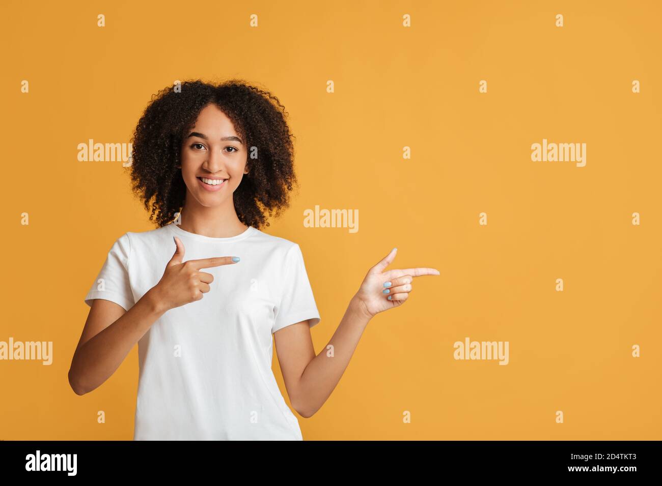 People sincere emotions, lifestyle and best choice concept. Cheerful african american lady in white t-shirt points fingers towards empty space Stock Photo
