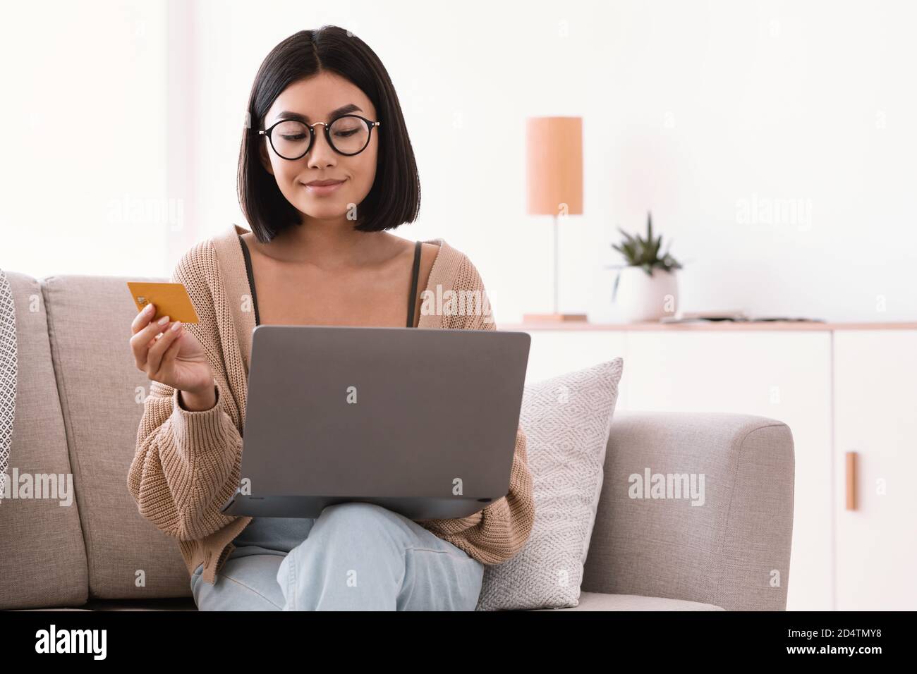 Asian woman making purchases sitting with pc on couch Stock Photo