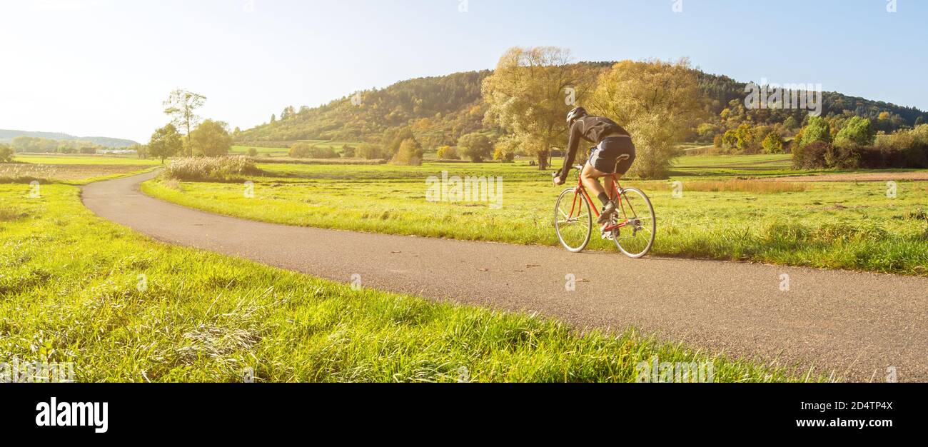 Panorama shot of cyclist on a racing bike in scenic rural autumn landscape during beautiful afternoon light Stock Photo