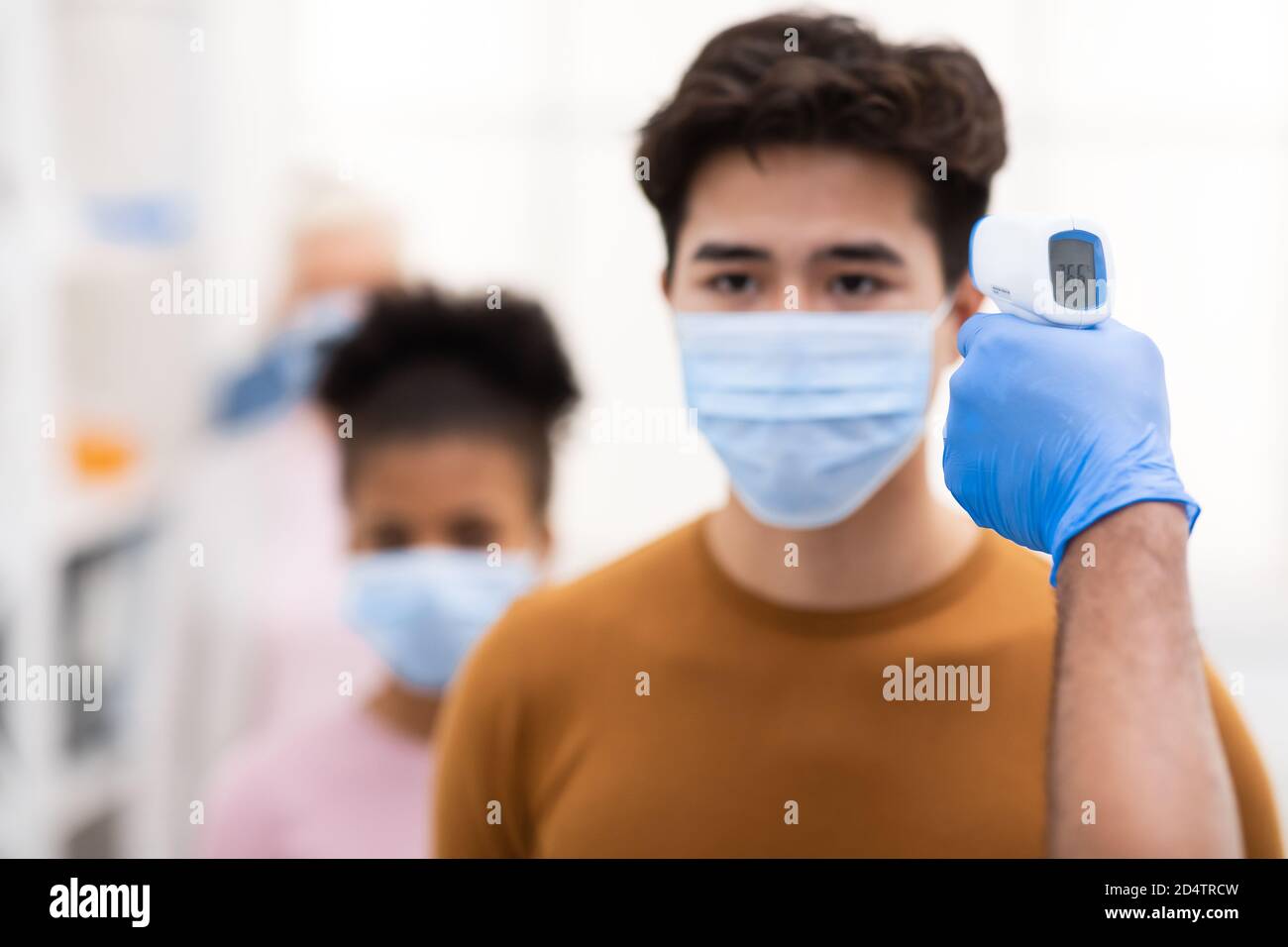 Medical Worker Doing Temperature Screening For Asian Man Indoors Stock Photo