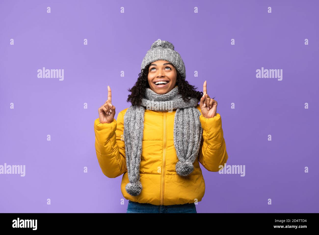 African Lady In Winter Jacket Pointing Fingers Upward, Purple Background Stock Photo