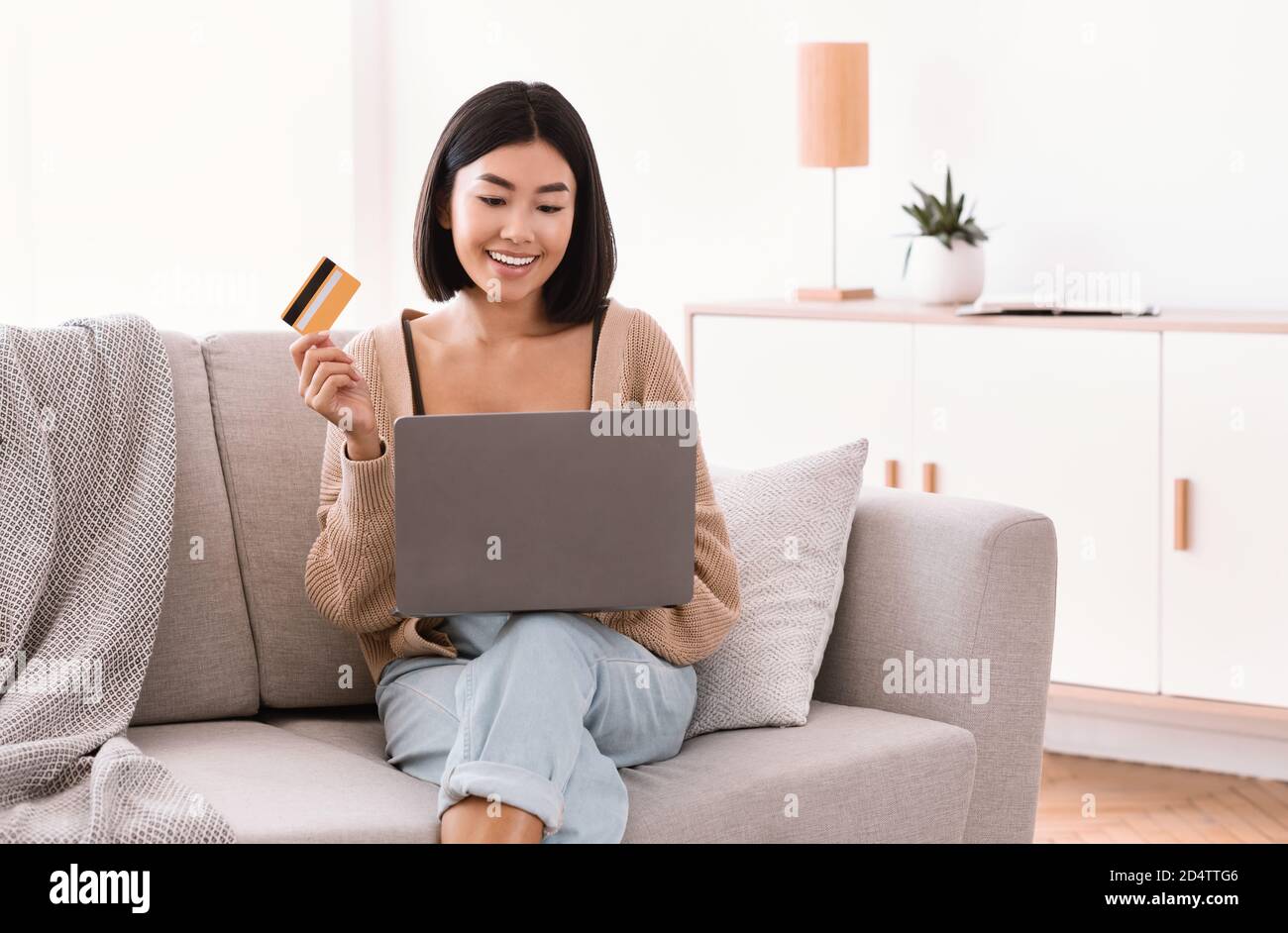 Young asian woman making purchases sitting with pc on sofa Stock Photo