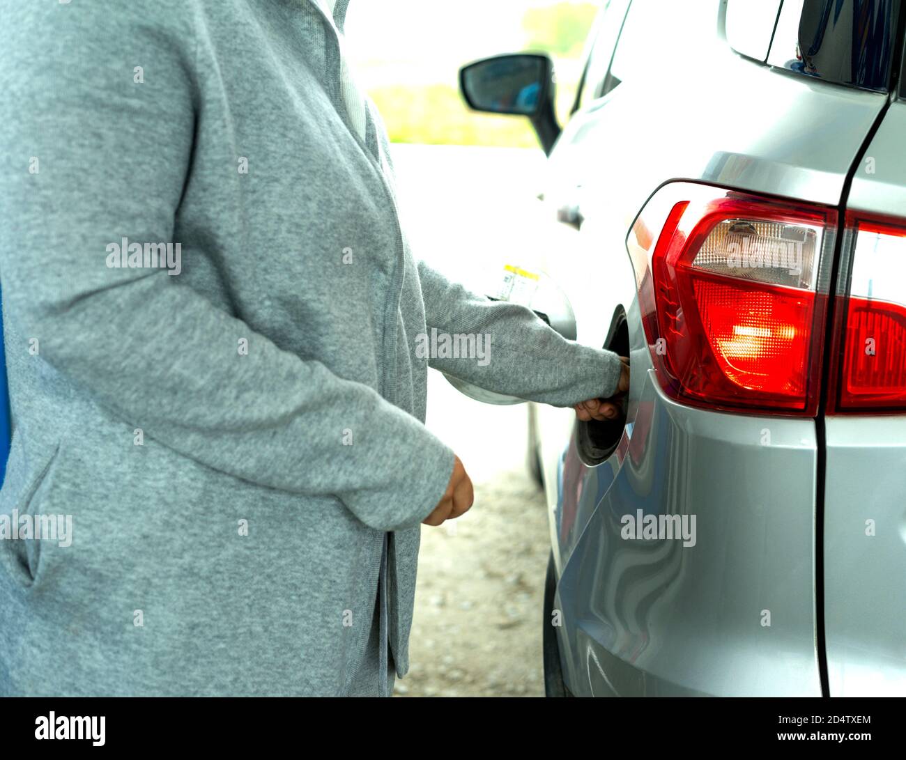 A woman's hand in a gray jacket opens the gas tank of a silver car at a
