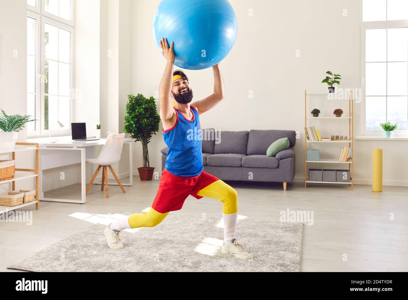 Cheerful bearded man in colorful sportswear doing sports workout with fitness ball at home Stock Photo