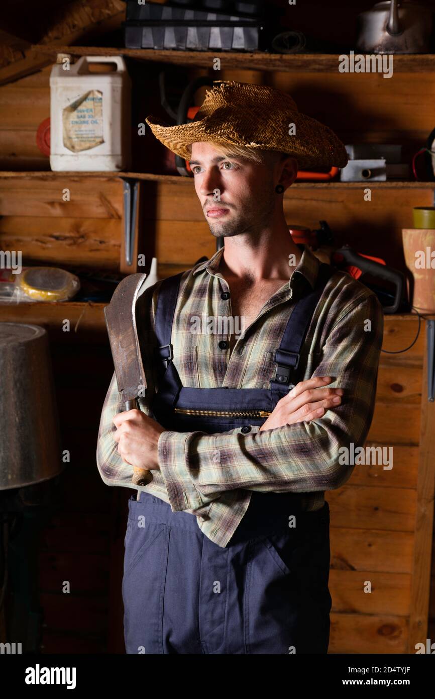 Young man in his 20s wearing dungarees and holding a billhook. Stock Photo