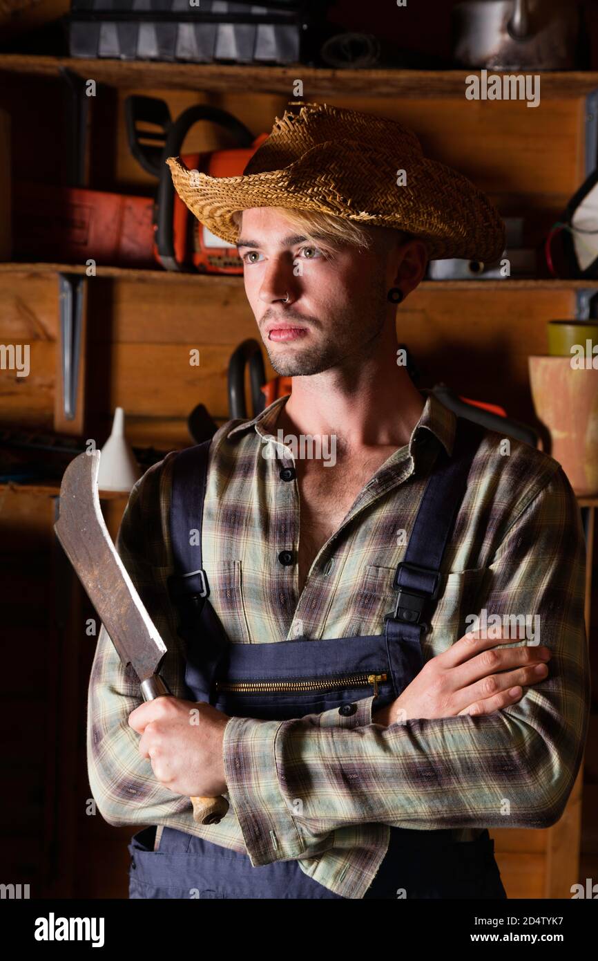 Young man in his 20s wearing dungarees and holding a billhook. Stock Photo
