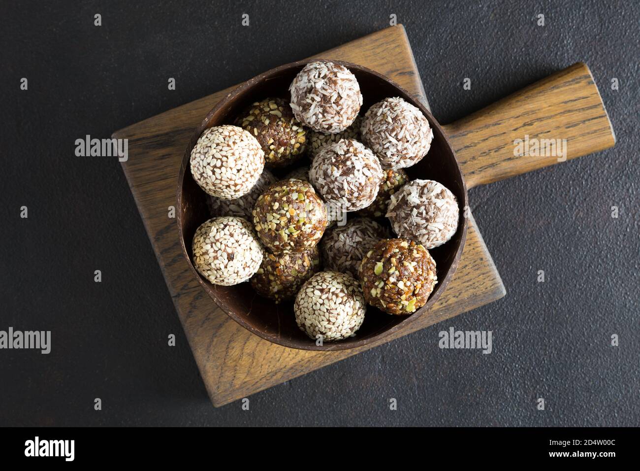 Raw vegetarian energy balls with cashews, hazelnuts and in the wooden bowl on board on dark background. Homemade, organic food. Flat lay, close up. Stock Photo