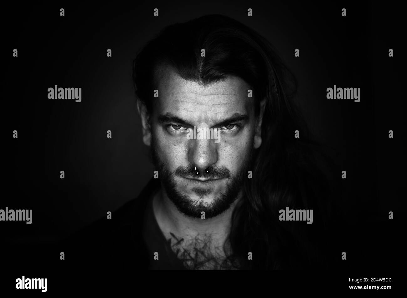 Man with long hair looks seriously and determined at the camera on an black and white image Stock Photo