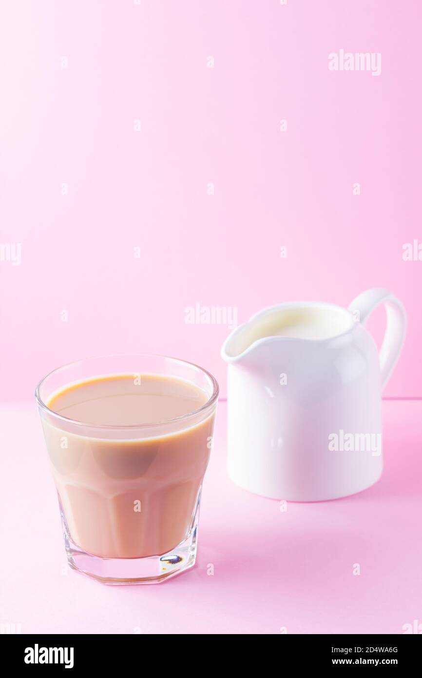 Milk tea on a pink background. Glass of masala chai tea and milk jug