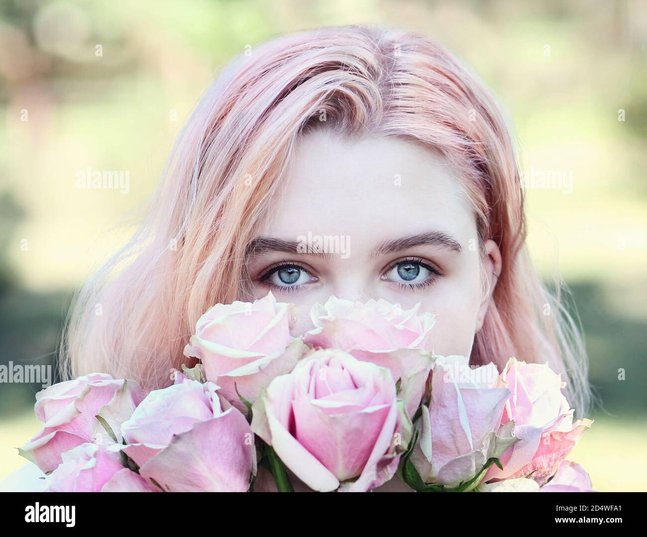 Beautiful girl with blue eyes sniffs pink roses, outdoors. Summertime. Stock Photo