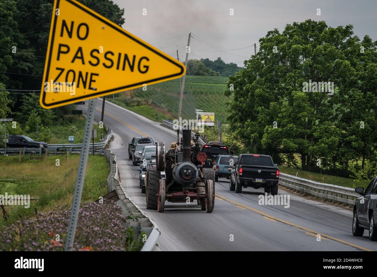 Two amish men slow traffic on no passing zone of highway with steam engine tractor. Stock Photo