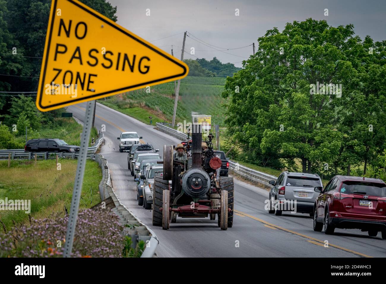 Two amish men slow traffic on no passing zone of highway with steam engine tractor. Stock Photo