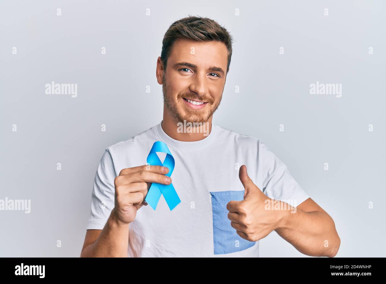 Handsome caucasian man holding blue ribbon smiling happy and positive ...