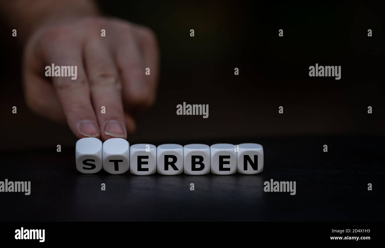 Hand turns dice and changes the German word 'sterben' (die) to 'erben' (inherit). Stock Photo