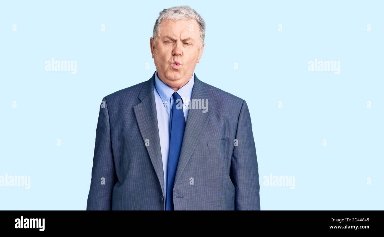 Senior grey-haired man wearing business jacket making fish face with ...