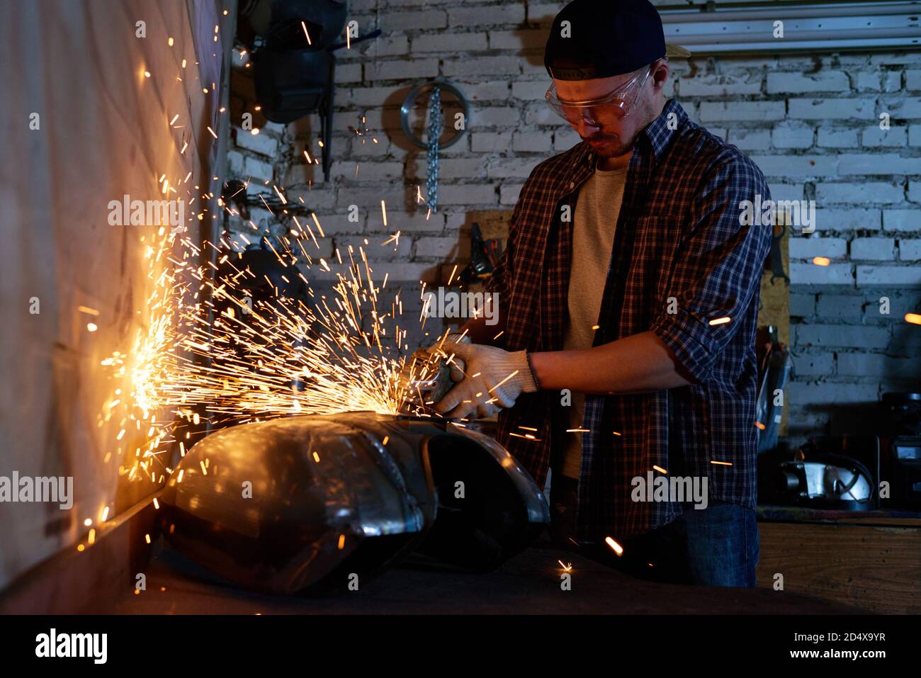 Young repairman grinding motorbike fuel tank part in his workshop Stock Photo