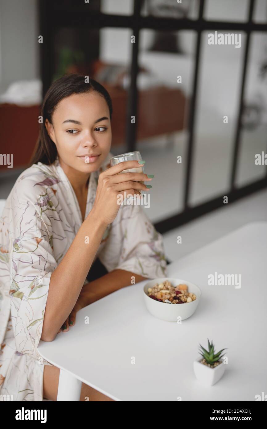 Beautiful young black female sitting at table eating breakfast and drinking coffee Stock Photo