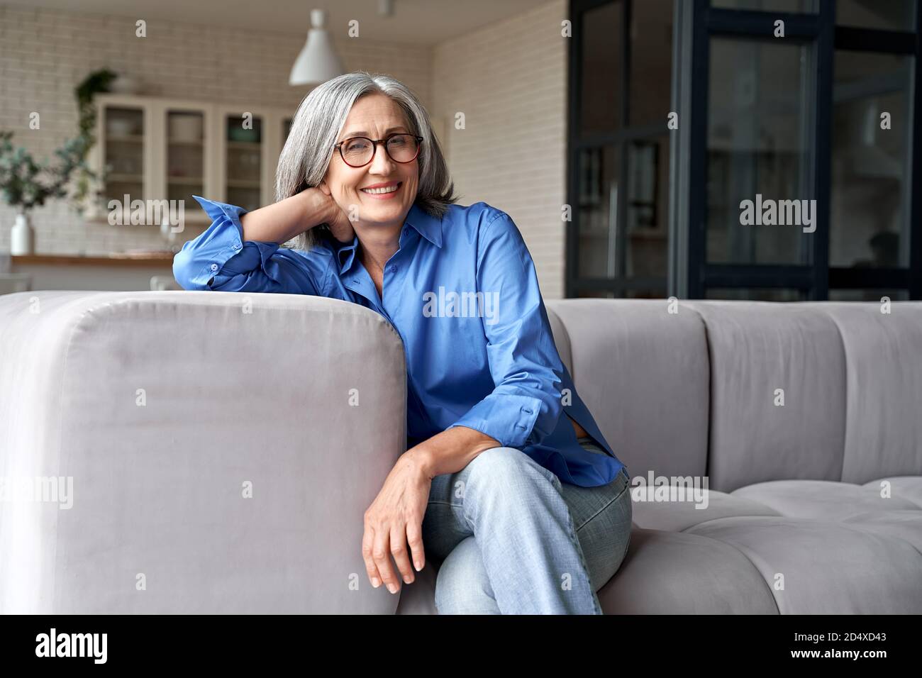 Happy relaxed mature old woman wears glasses sitting on couch at home, portrait. Stock Photo