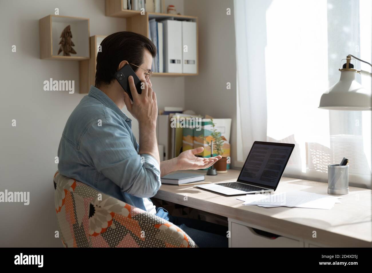 Young man working on computer with documents, talking on phone. Stock Photo