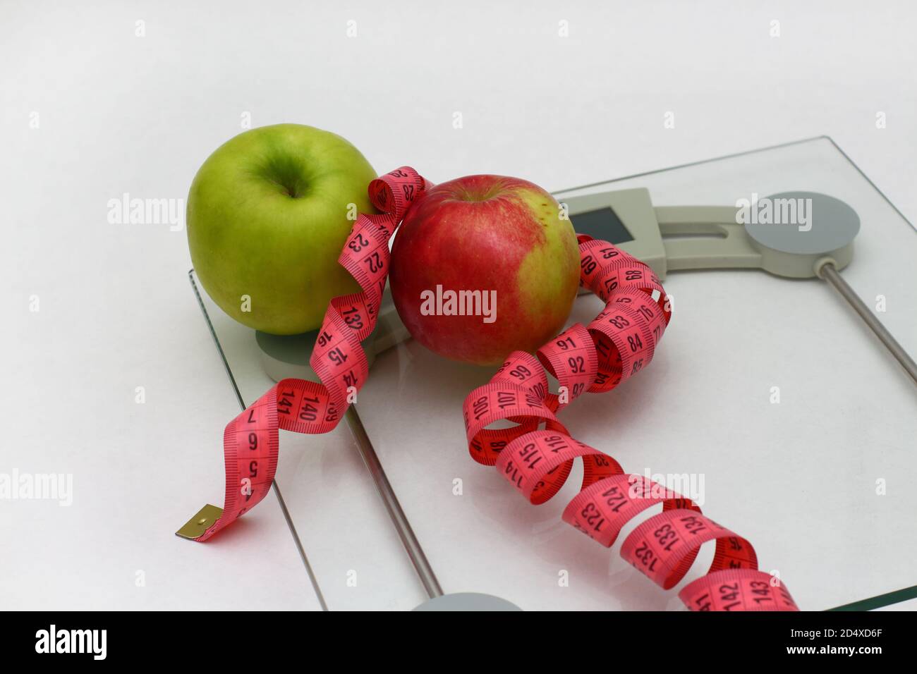 https://c8.alamy.com/comp/2D4XD6F/two-fresh-apples-green-and-red-with-pink-measuring-ribbon-lie-on-glass-floor-scales-white-background-2D4XD6F.jpg