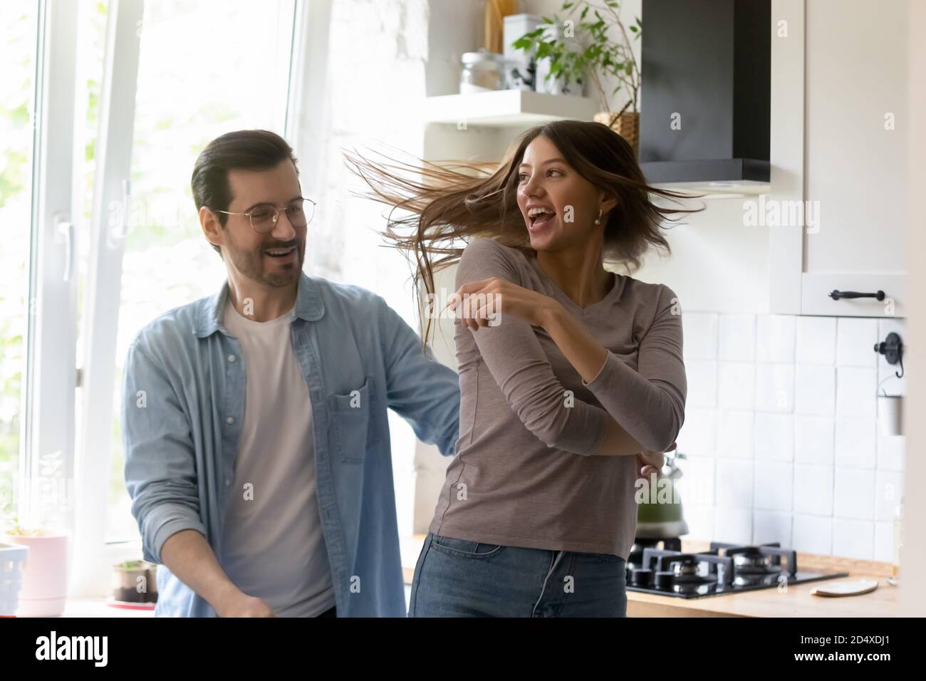 Emotional playful young family couple dancing in kitchen. Stock Photo