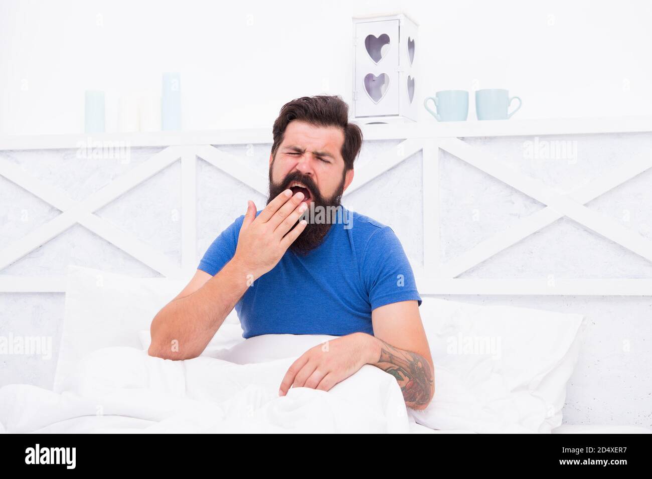 Lethargic tired man sitting in bed yawning as he struggles to wake up unmotivated to start the new day, early morning routine. Stock Photo