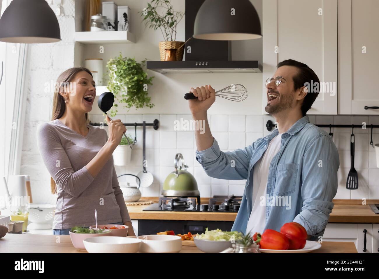Overjoyed funny family spouses singing songs in kitchen utensils Stock