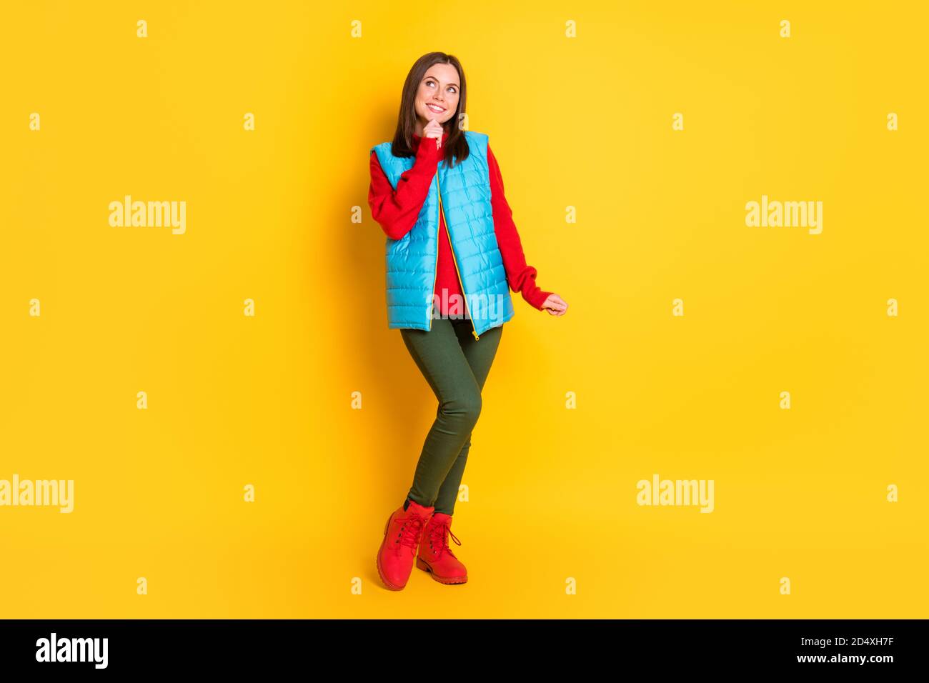 Full body size photo of pretty cute young lady dreamy look empty space hand chin smiling girlish posing wear green pants blue vest red sweater boots Stock Photo