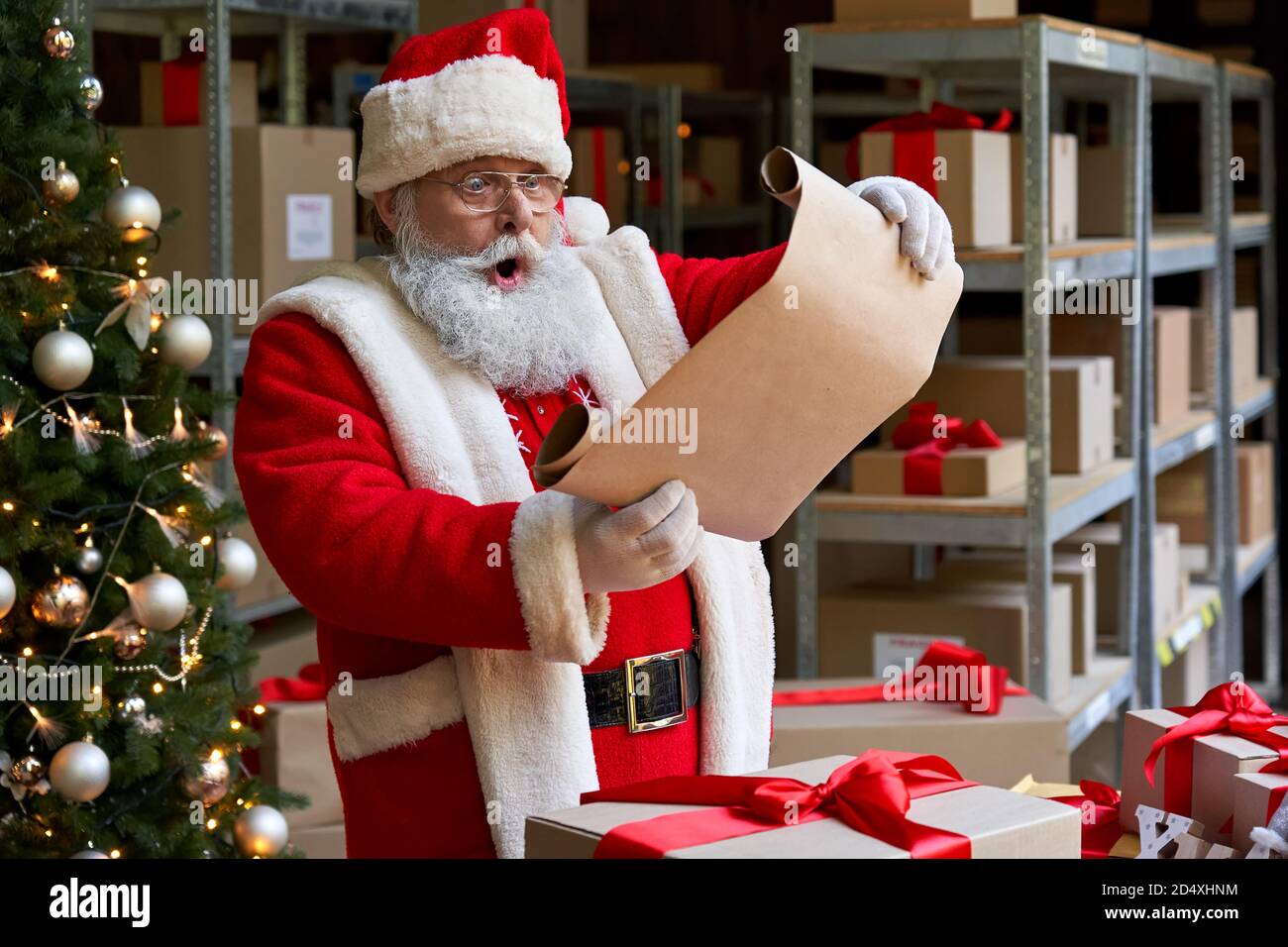 Shocked Santa Claus wearing costume reading wish list standing in workshop. Stock Photo