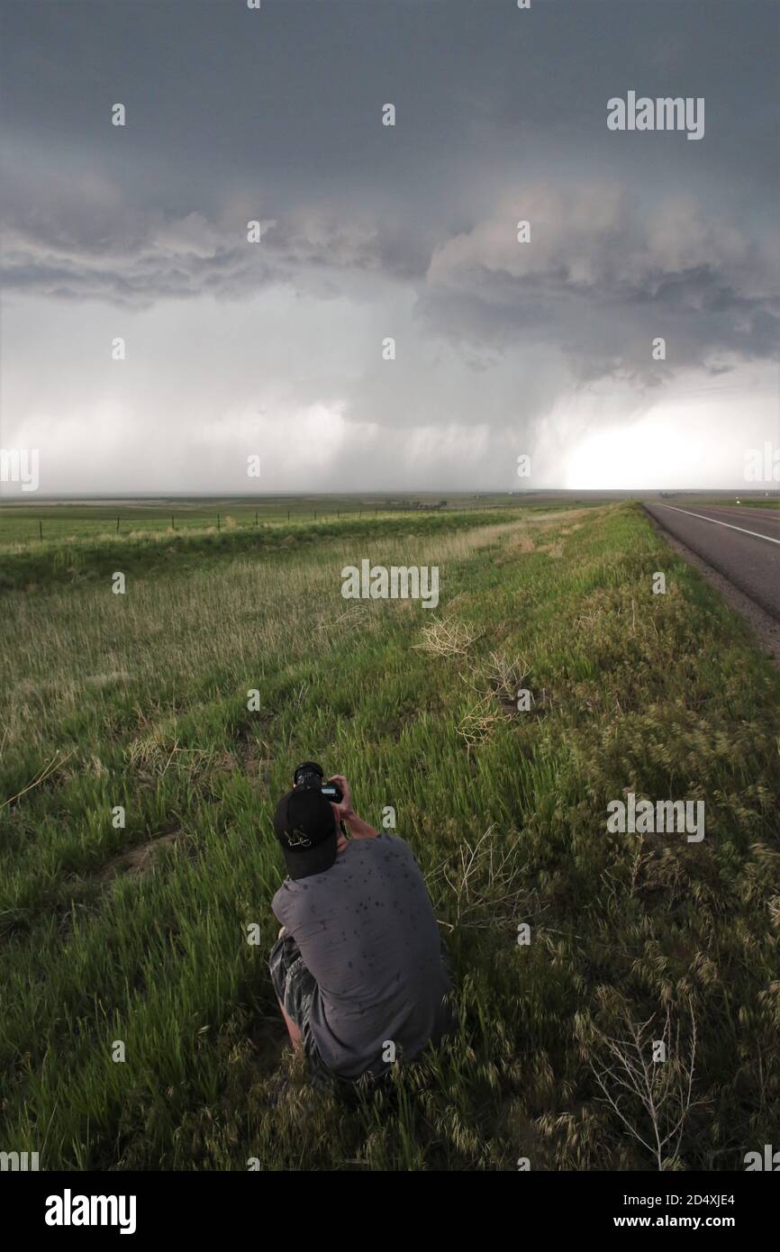 A man crouching on the ground and photographing a storm in the distance. Stock Photo