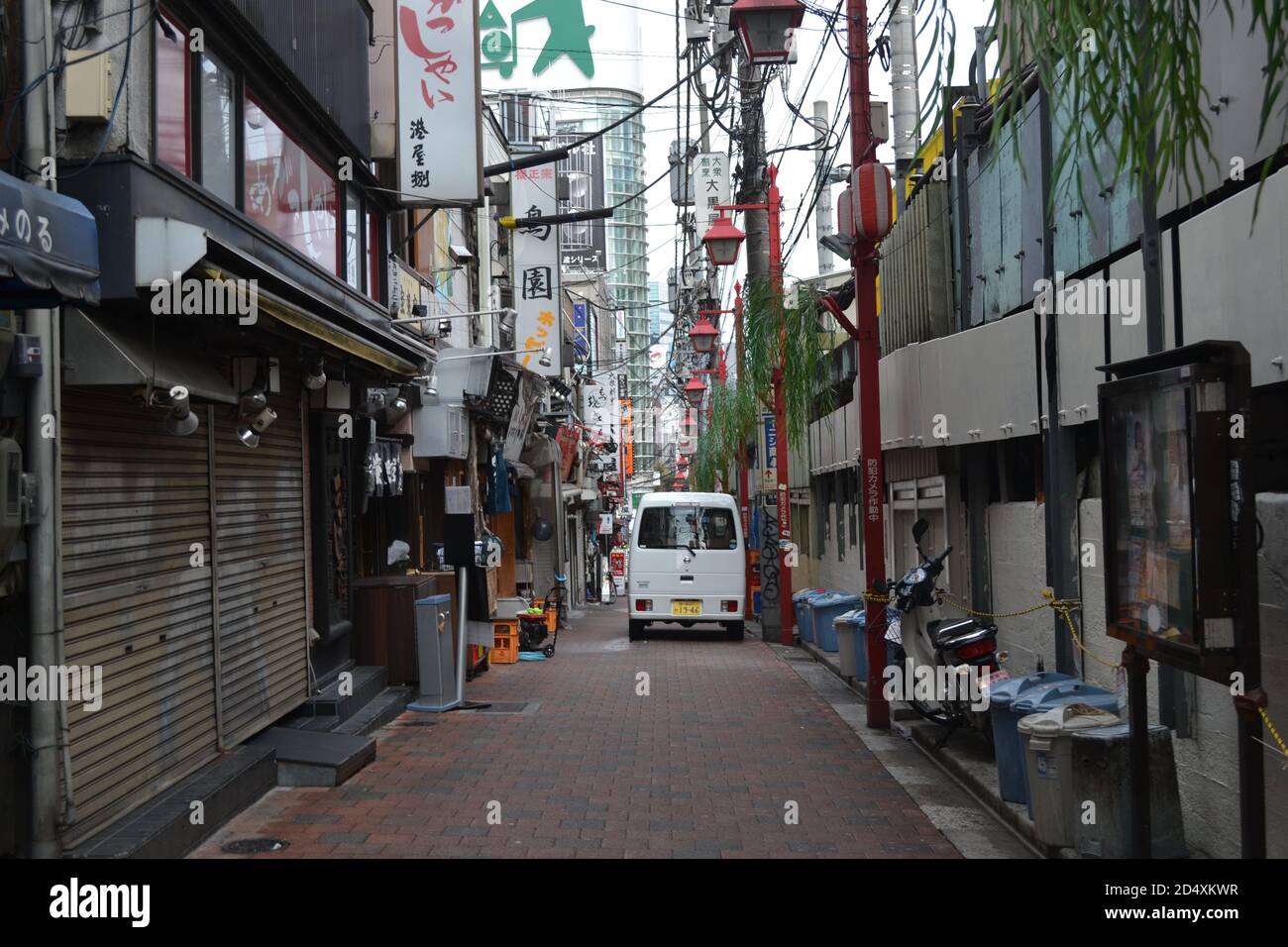 Tokyo, Japan-2/24/16: Small Japanese van drives down a condensed alley in Tokyo with various restaurants, food chains, and shops on the side. Stock Photo