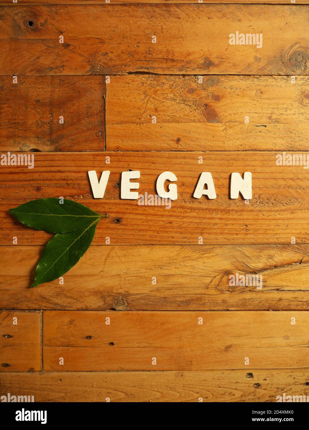 Word 'VEGAN' in white letters on a wooden background with two laurel leaves Stock Photo