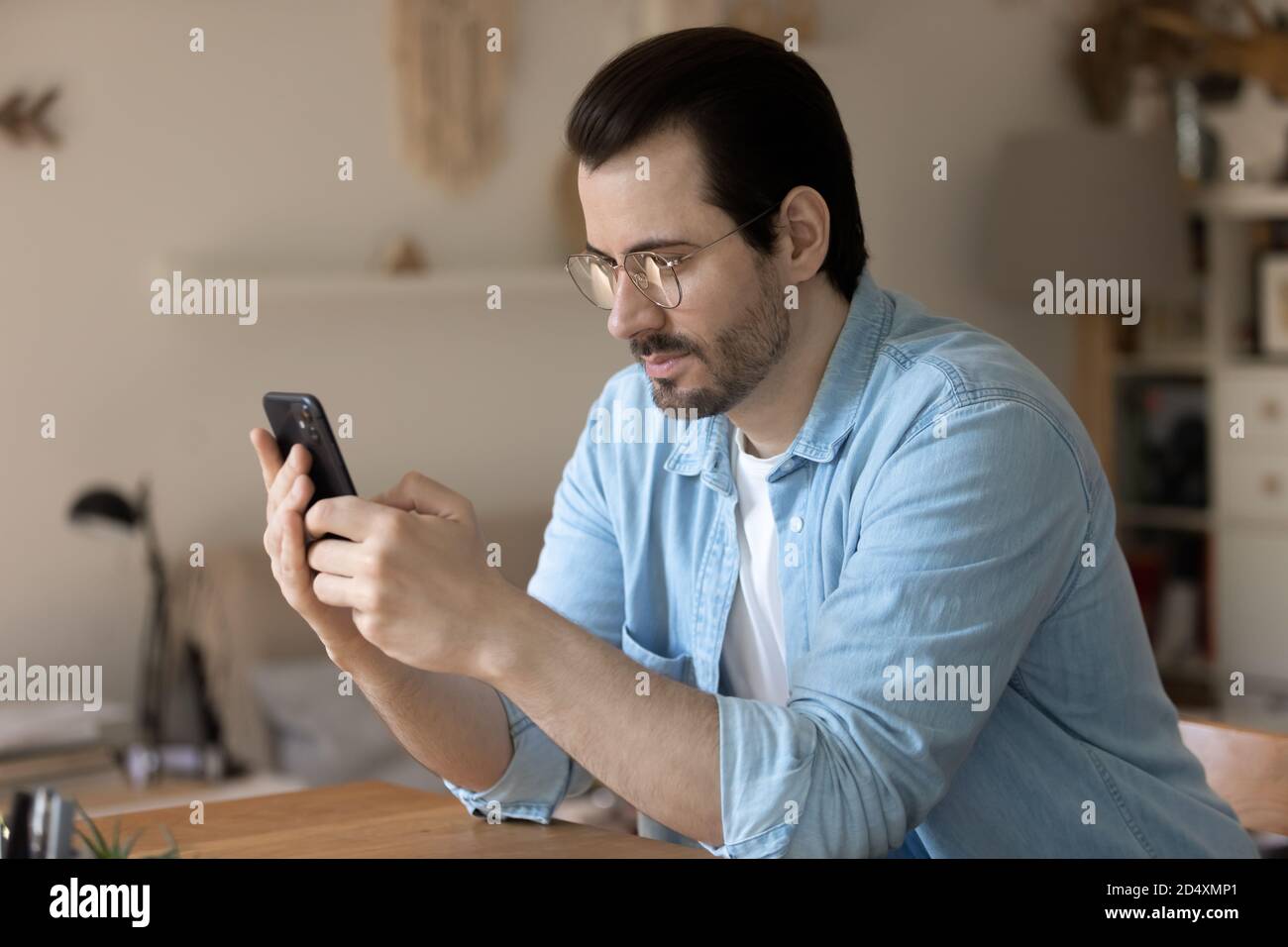 Pleased young handsome man using mobile application at home. Stock Photo